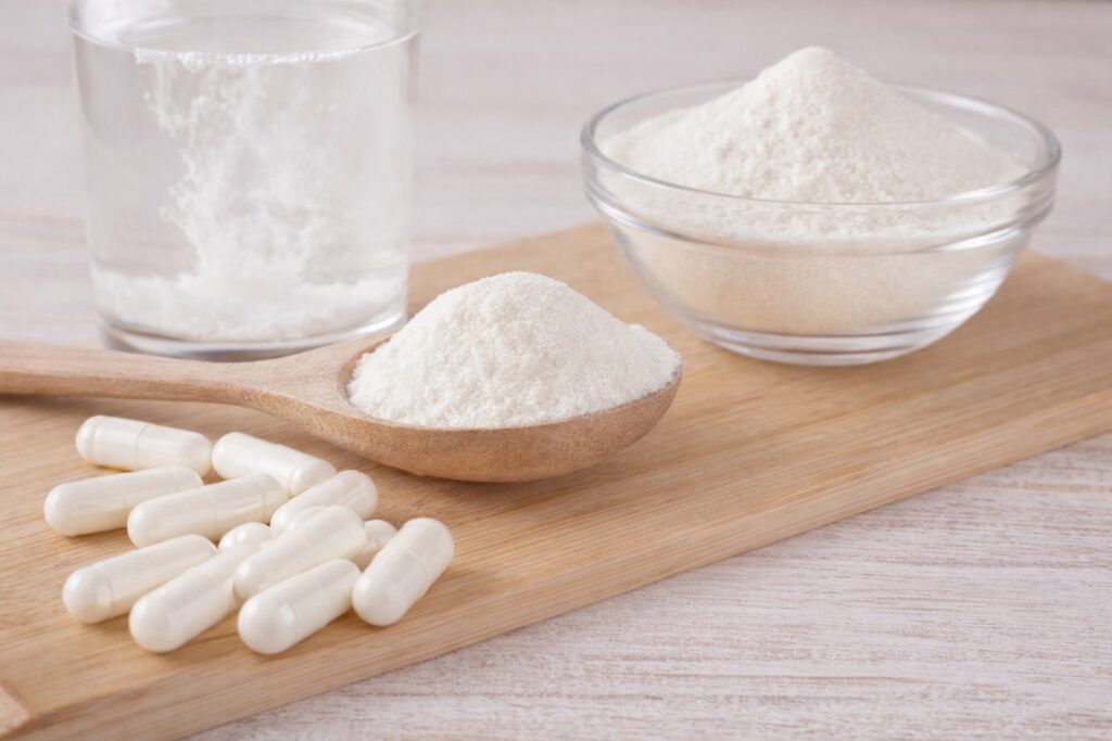 suplemento de colágeno hidrolisado em pó e cápsulas sobre superfície de madeira
